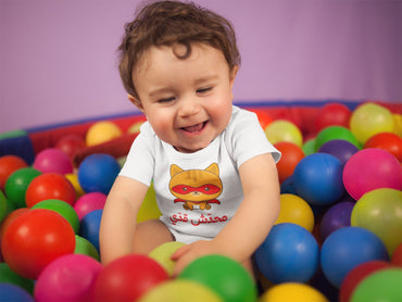 Laughing baby in a white محدش قدي superhero cat Arabic onesie in a ball pit