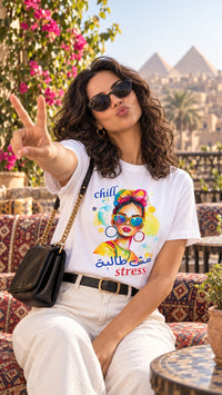 Woman wearing the white Chill مش طالبة stress Arabic pop art tee with white jeans on a terrace overlooking the Giza pyramids