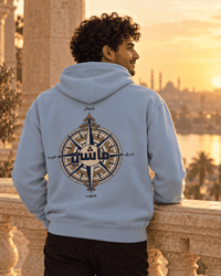 Man wearing the ماشي compass Arabic hoodie in Carolina Blue at sunset over Cairo, by Cairo NYC