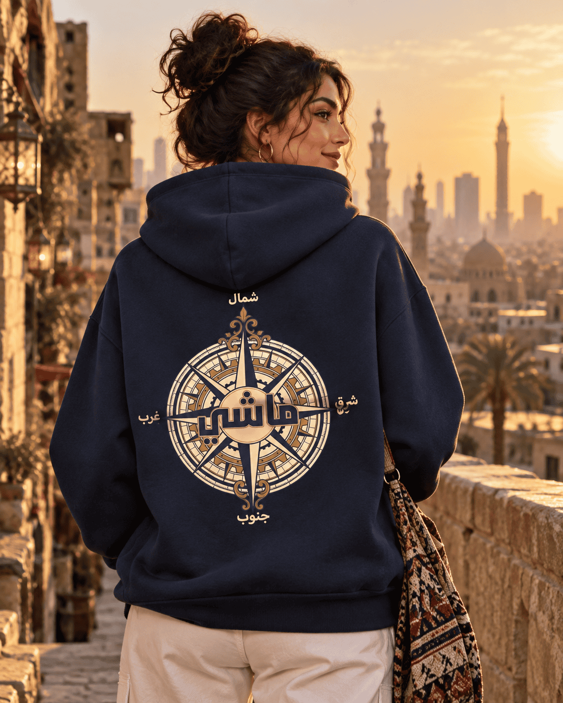 Woman wearing the ماشي compass Arabic hoodie in Navy overlooking Cairo minarets at sunset, by Cairo NYC
