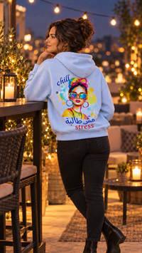 Woman wearing the Chill مش طالبة stress Arabic pop art hoodie with black jeans and ankle boots on a rooftop at night