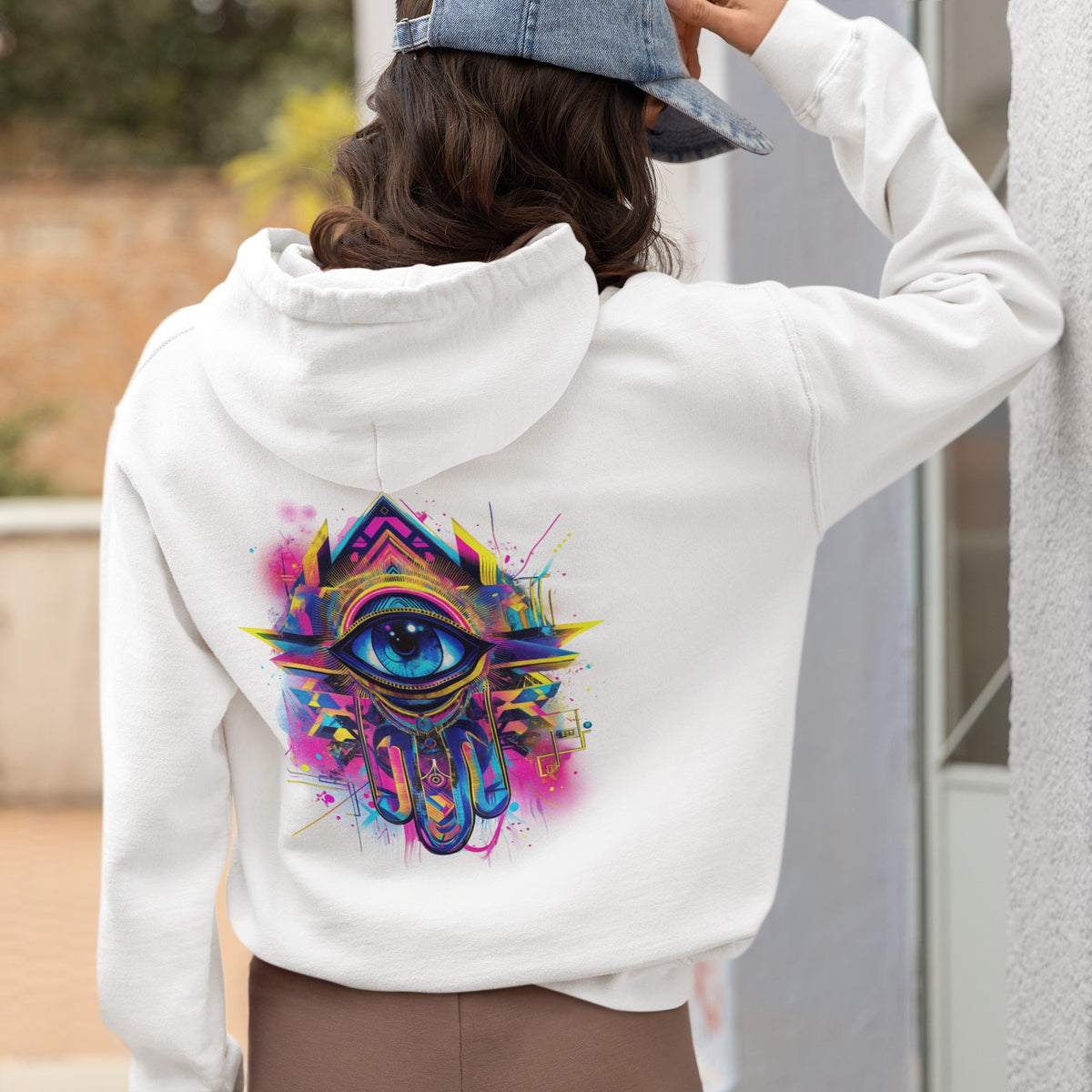 Back view of a white hoodie with a colorful khamsa evil eye protection design, styled with a denim cap