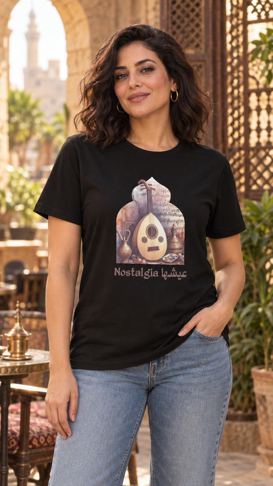 Woman in a black Nostalgia عيشها oud Arabic tee and light jeans in an Old Cairo courtyard