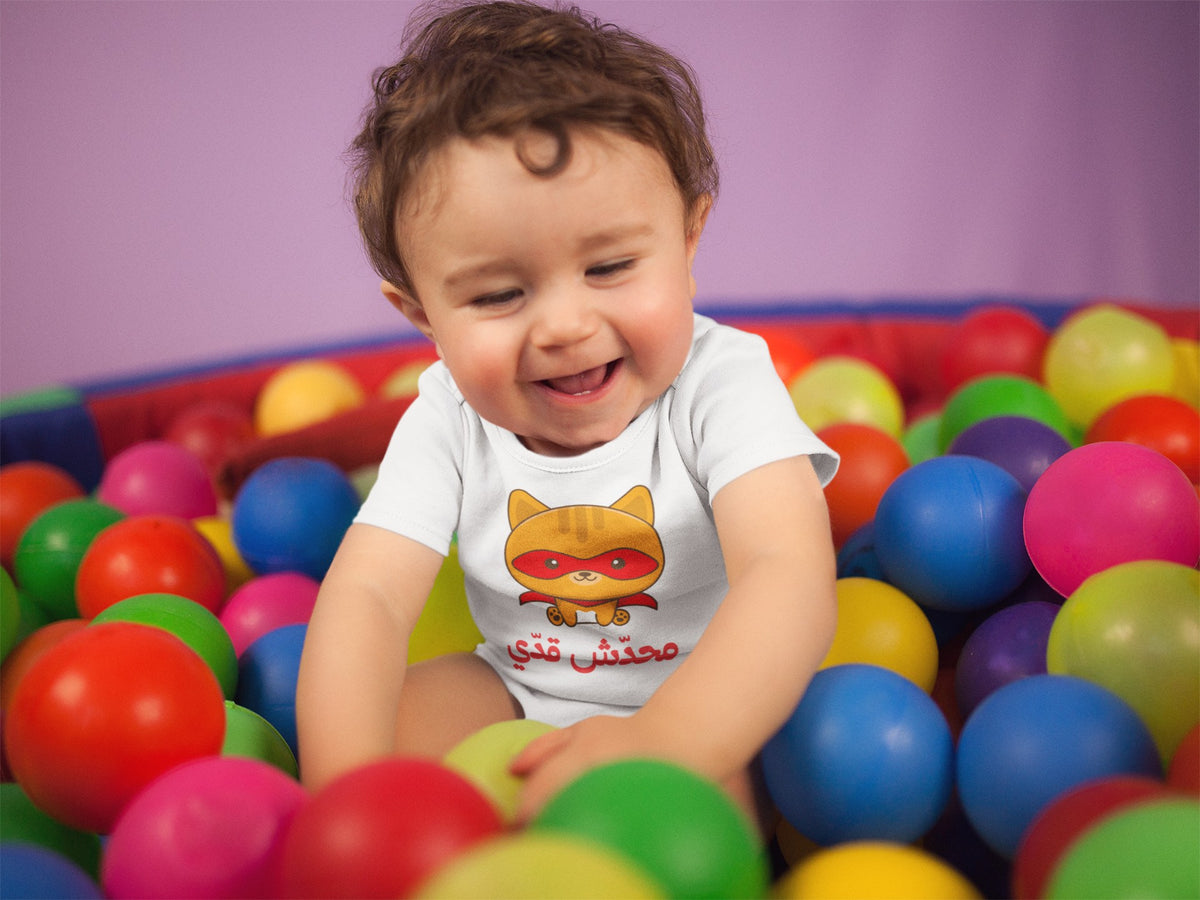 Laughing baby in a white محدش قدي superhero cat Arabic onesie in a ball pit